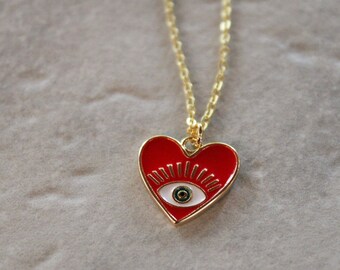 May include: Gold chain necklace with a red heart pendant featuring a white eye with a green iris.
