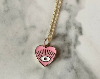 May include: A gold chain necklace with a pink heart pendant featuring a black evil eye design.