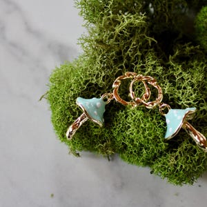 May include: Two gold mushroom charms with blue and white enamel. The charms are attached to a gold chain.