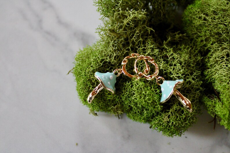 May include: Two gold mushroom charms with blue and white enamel. The charms are attached to a gold chain.
