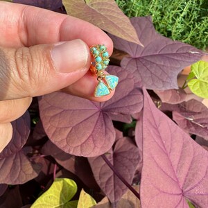 May include: Gold hoop earrings with turquoise and opal stones. The earrings are dangling and have a triangular shape.
