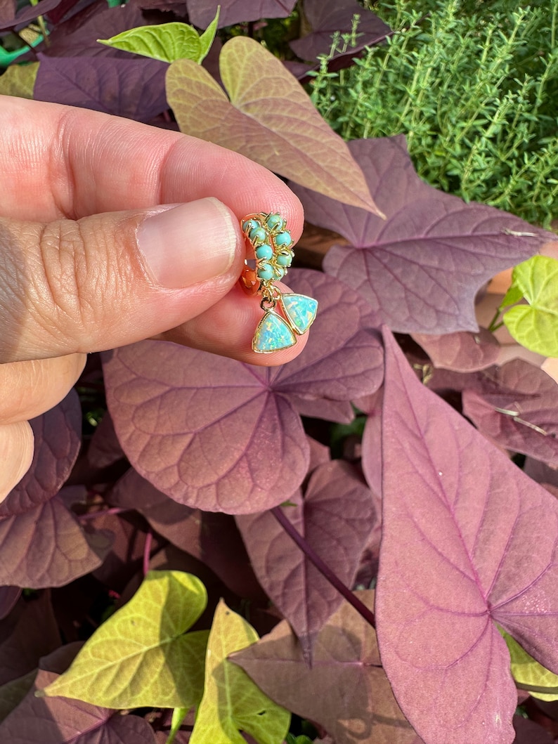 May include: Gold hoop earrings with turquoise and opal stones. The earrings are dangling and have a triangular shape.