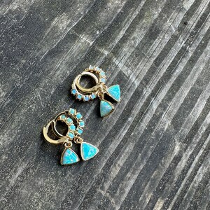 May include: A pair of gold hoop earrings with a circle of small blue opal stones and a dangling triangle-shaped blue opal stone.