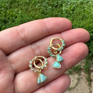May include: A pair of gold hoop earrings with a dangling triangle-shaped opal gemstone. The hoops are adorned with small white opal stones.