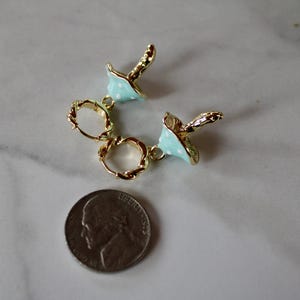 May include: A pair of gold hoop earrings with blue and white enamel mushroom charms. The charms are attached to the hoops with gold jump rings.