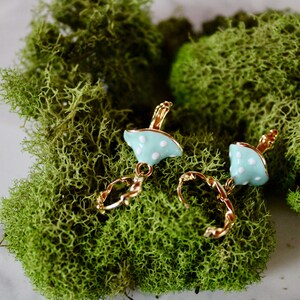 May include: A pair of gold hoop earrings with a light blue mushroom charm. The mushroom charm has white polka dots.