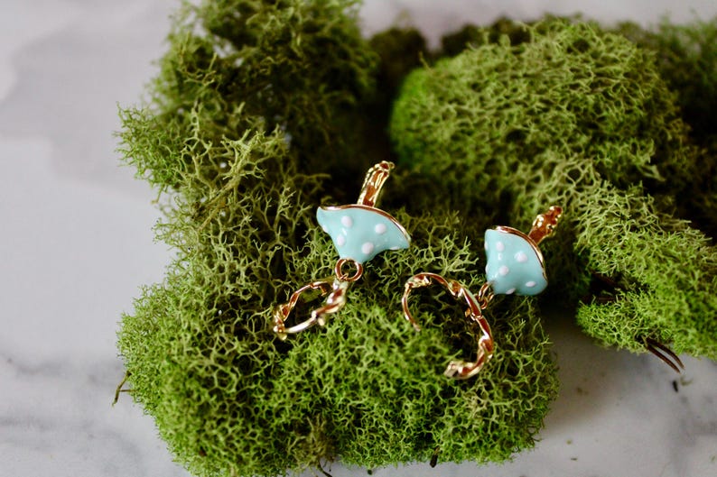 May include: A pair of gold hoop earrings with a light blue mushroom charm. The mushroom charm has white polka dots.