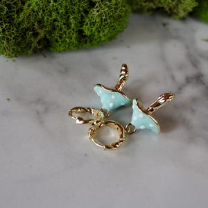 May include: A pair of gold hoop earrings with a light blue mushroom charm with white polka dots hanging from each hoop.