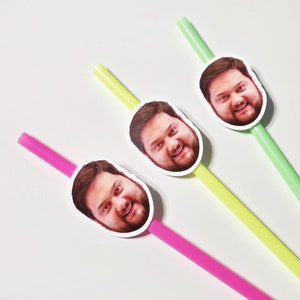May include: Three colorful drinking straws with a photo of a person's face on each straw. The straws are pink, yellow, and green.