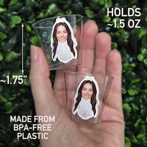 May include: Two clear plastic shot glasses, each featuring a sticker of a person wearing a white bridal veil. The cups are 1.75 inches tall, hold 1.5 ounces, and are made from BPA-free plastic. The design shows a smiling face with long brown hair.