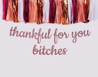 May include: A decorative banner featuring a row of hanging tassels in shades of burgundy, peach, white, and metallic copper. Below the tassels, the text "thankful for you bitches" is displayed in a rose gold glittery cursive font on a plain background.