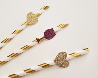 May include: Three gold and white striped paper straws with decorative embellishments. One straw has a gold glitter heart, one has a burgundy glitter wine glass, and one has a gold glitter heart.