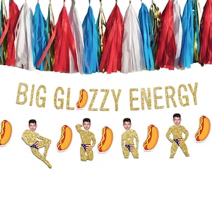 May include: A festive banner with the text "BIG GLOZZY ENERGY" in gold glitter letters. The banner includes cutouts of a person in a gold suit and hot dogs. Colorful tassel garland hangs above.