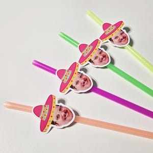 May include: Four colorful straws with attached face cutouts wearing pink sombreros. The straws are in shades of pink, green, and yellow. The sombreros have yellow and green decorative patterns. The face cutouts have glasses and a smiling expression.