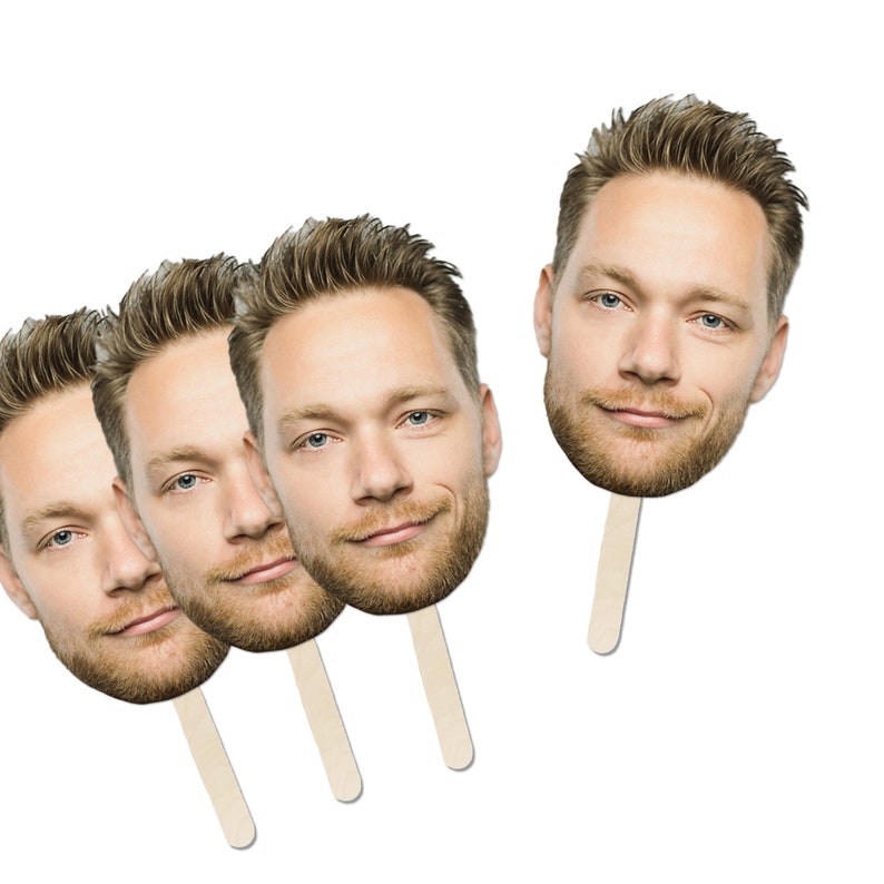 May include: Four cardboard face cutouts on sticks, featuring a man with brown hair and a beard. The cutouts are arranged in a row, with the sticks pointing upwards.