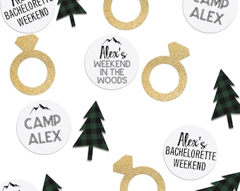 Puede incluir: Esparcidos sobre un fondo blanco hay varias decoraciones de fiesta, incluyendo árboles de cuadros verdes y negros, anillos de purpurina dorada y círculos blancos con texto negro. El texto en los círculos dice "Alex's Bachelorette Weekend", "Camp Alex" y "Alex's Weekend in the Woods".