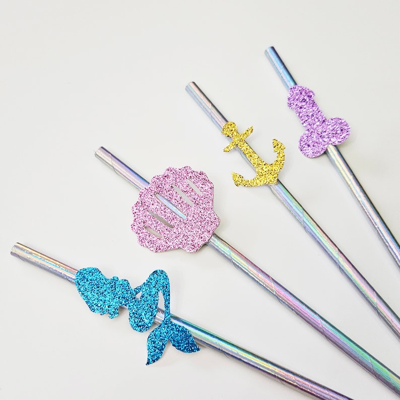 Op de afbeelding: Vier regenboogkleurige drinkrietjes met glitteraccenten. De rietjes hebben een zeemeermin, schelp, anker en een paarse vorm.