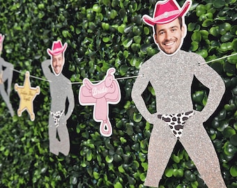 May include: A string of glittery cowboy-themed cutouts, including a sheriff's star, a pink saddle with the word "Bride", and male figures wearing cowboy hats and swim briefs. The background is a wall of green foliage.