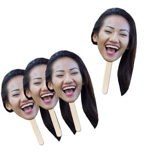 May include: Four paper face cutouts on sticks, featuring a woman with long dark hair laughing. The cutouts are printed with a photo of the woman's face.