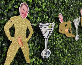 May include: A decorative garland featuring gold glitter cutouts of figures with attached photographic faces, each wearing a hot dog graphic, interspersed with illustrations of martini glasses containing green olives on a white string.
