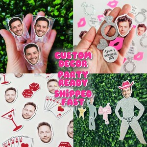May include: Custom party decorations featuring personalized face cutouts on clear shot glasses, glittery silver engagement ring shapes, heart confetti, playing cards, dice, and a glittery silver cutout of a person wearing a pink cowboy hat.