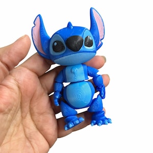Peut inclure: Un jouet articul&eacute; Stitch bleu et rose. Le jouet est en position debout, les bras le long du corps.