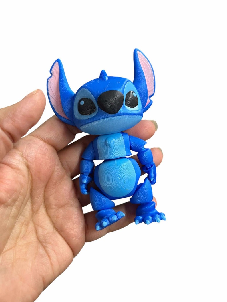 Peut inclure: Un jouet articul&eacute; Stitch bleu et rose. Le jouet est en position debout, les bras le long du corps.