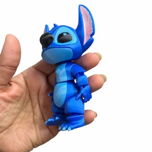 Peut inclure: Une figurine en 3D imprim&eacute;e en bleu et rose de Stitch du film Disney Lilo & Stitch. La figurine est en position debout, les bras le long du corps.