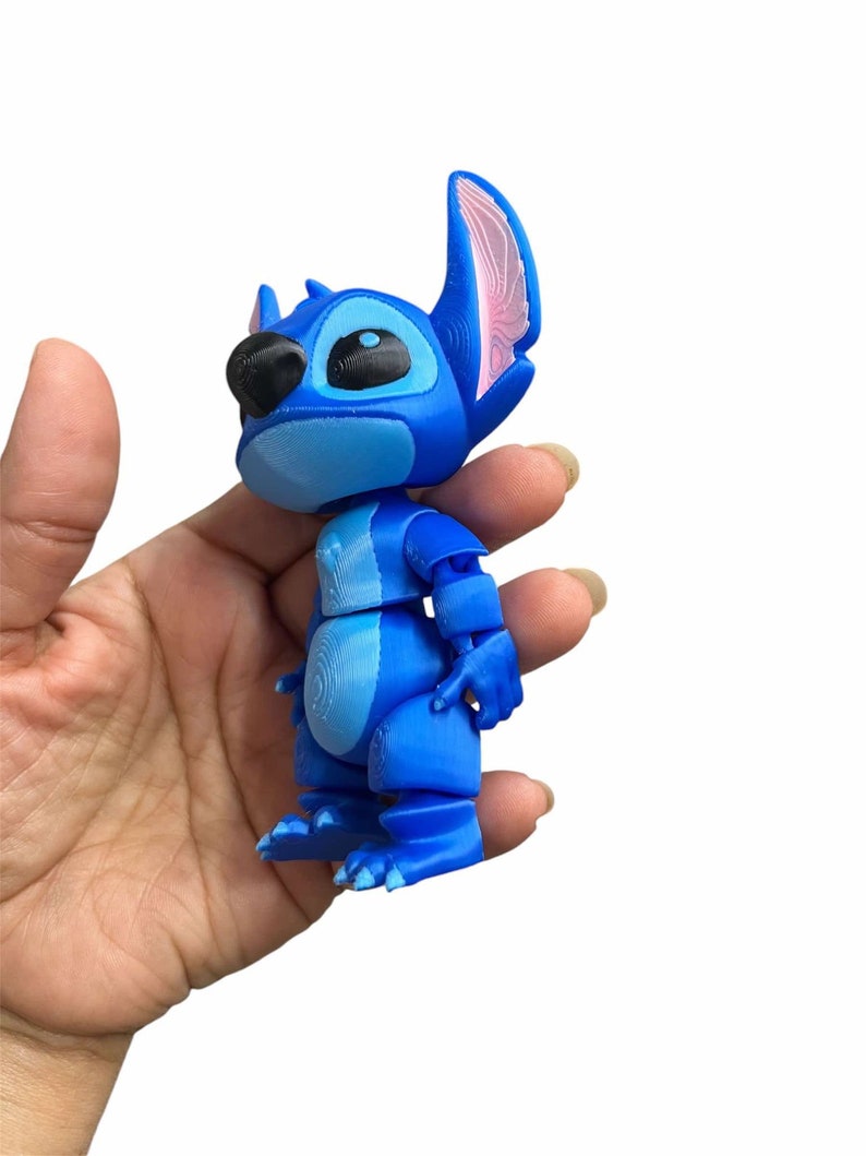 Peut inclure: Une figurine en 3D imprim&eacute;e en bleu et rose de Stitch du film Disney Lilo & Stitch. La figurine est en position debout, les bras le long du corps.