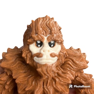 May include: A brown, furry creature with a white face and large, black eyes. The creature has a long, brown beard and a small, white nose.