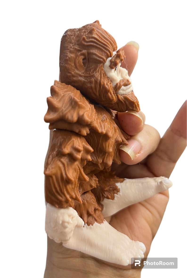 May include: A brown and white 3D printed figurine of a mythical creature, possibly a Bigfoot or Yeti, with a hairy body and a human-like face. The figurine is sitting with its legs crossed and its arms folded.