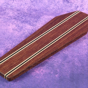 May include: A wooden, rectangular object with a dark brown finish. Two parallel, thin stripes of white and black run along the length of the object. The item is set against a purple background.