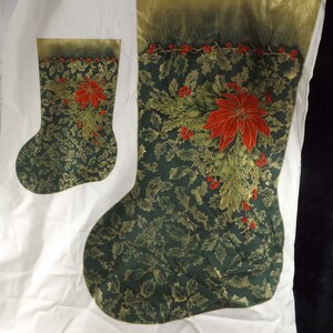 May include: Two Christmas stockings. The larger stocking is dark green with a gold pattern of leaves and holly. A red poinsettia and berries are centered on the stocking. The top is gold with red berries. The smaller stocking has the same design.