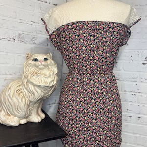 May include: A black floral print dress with a white lace overlay on the top. The dress has short sleeves and a fitted bodice.
