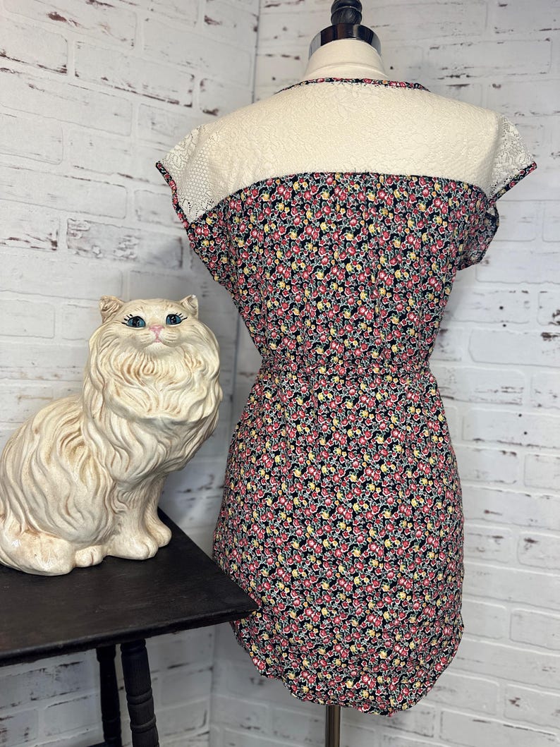 May include: A black floral print dress with a white lace overlay on the top. The dress has short sleeves and a fitted bodice.