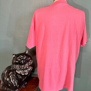 May include: A pink t-shirt on a mannequin. The t-shirt is plain with no visible graphics or text.