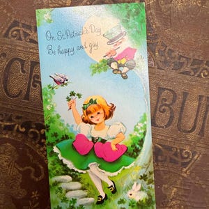 May include: Vintage St. Patrick's Day greeting card with a whimsical illustration. The card features a young girl in a green dress holding a four-leaf clover, a leprechaun, and the text "On St. Patrick's Day, Be happy and gay."