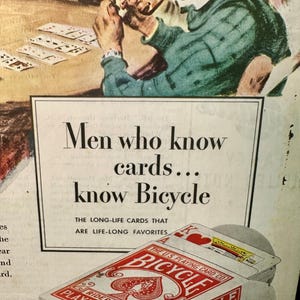 Może przedstawiać: Reklama w stylu vintage dla kart do gry Bicycle. Obraz przedstawia talię kart z czerwono-białym wzorem i tekstem "Men who know cards... know Bicycle". Reklama pokazuje r&oacute;wnież grupę ludzi grających w karty.