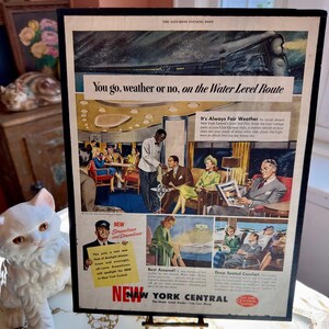 May include: Framed vintage advertisement from The Saturday Evening Post. The ad promotes the New York Central Railroad's Water Level Route. The ad features illustrations of passengers enjoying the train's amenities, with text that reads "You go, weather or no."