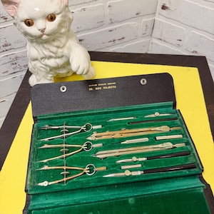 May include: A vintage Charles Bruning Company No. 1050 Majestic drafting set in a black case with a green velvet interior. The set includes various metal compasses, dividers, and drawing tools with metallic finishes, arranged in custom-molded slots.