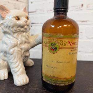 May include: A vintage amber glass bottle with a black cap and a label that reads "Norda Essential Oil Orange CP USP." The label has a green and gold border and a logo. The bottle's net weight is 1 lb.