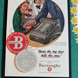 May include: Vintage advertisement for Burroughs adding machines. The image features a retro-style illustration with a dark-colored adding machine, and three people. The text reads "Here's the tag that tells the story" and "Burroughs".