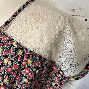 May include: A black dress with a floral print and a white lace overlay on the shoulders.