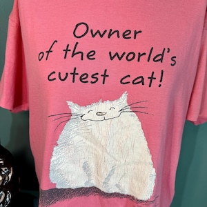 May include: Pink t-shirt with a white cat illustration and the text "Owner of the world's cutest cat!"