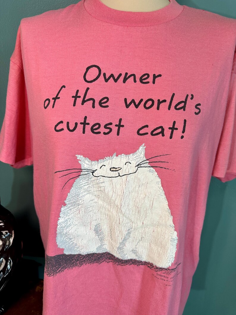 May include: Pink t-shirt with a white cat illustration and the text "Owner of the world's cutest cat!"