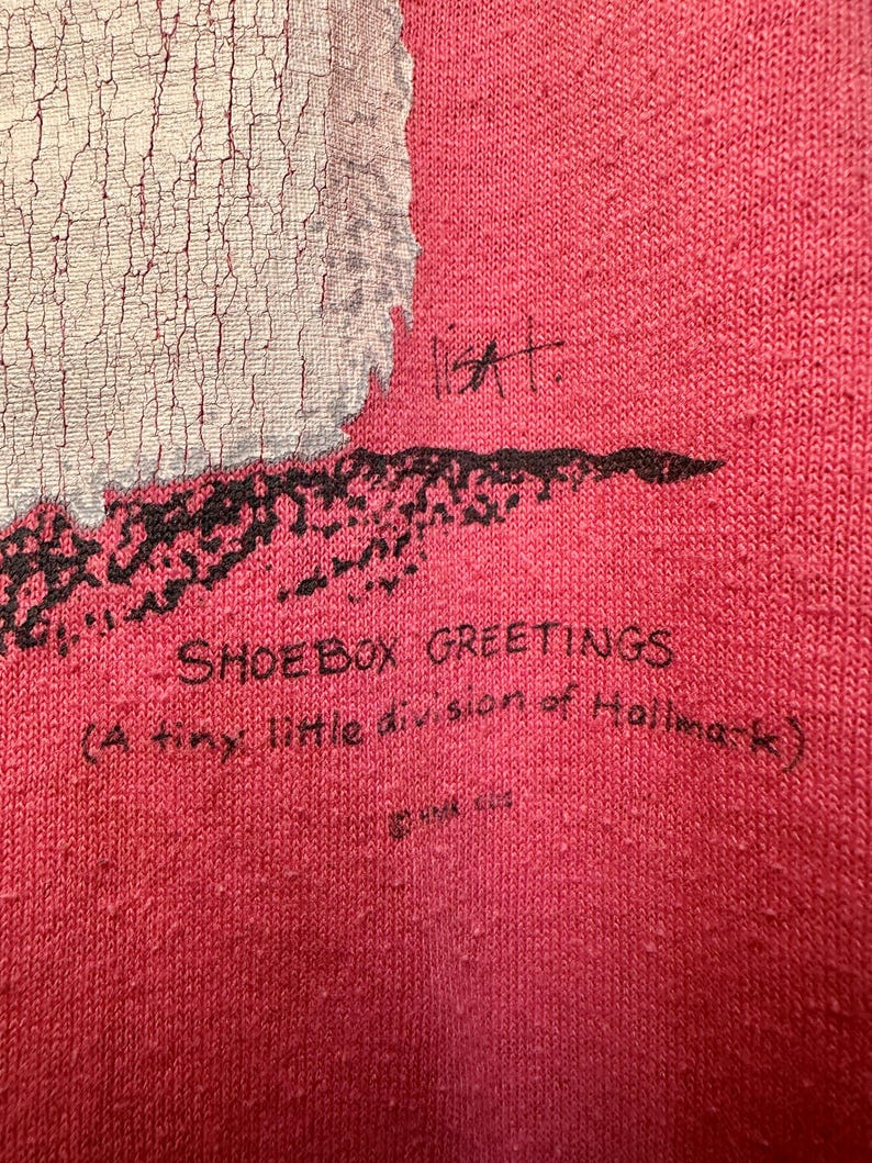 May include: Red t-shirt with a white and black graphic print of a snowman. The text "Shoebox Greetings (A tiny little division of Hallmark)" is printed on the bottom of the shirt.
