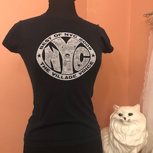 May include: Black t-shirt with a white circle graphic featuring the text "Best of NYC 2009 The Village Voice" and a stylized illustration of the NYC skyline.