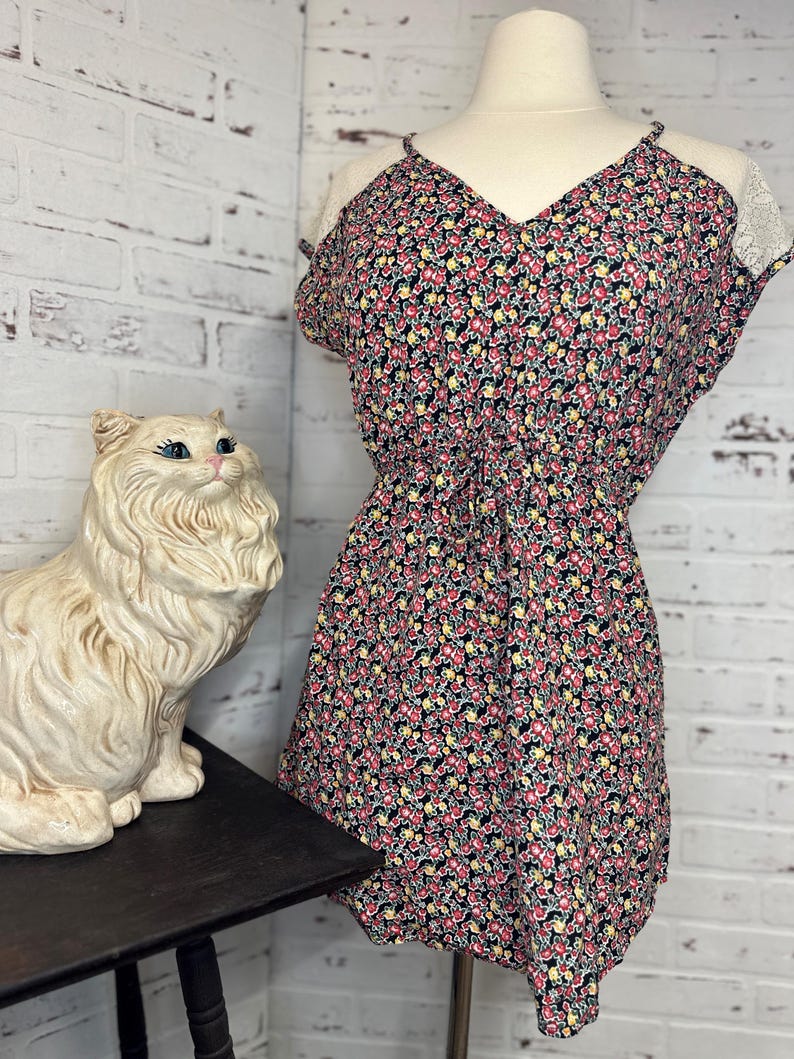 May include: A black floral print dress with a V-neckline and lace trim on the shoulders. The dress has a fitted bodice and a flowy skirt.