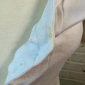 May include: Close-up of a light yellow and off-white long-sleeved shirt. The shirt has a buttoned placket and a light blue collar. There are yellow stains on the collar and sleeve. The fabric appears to be a soft knit.