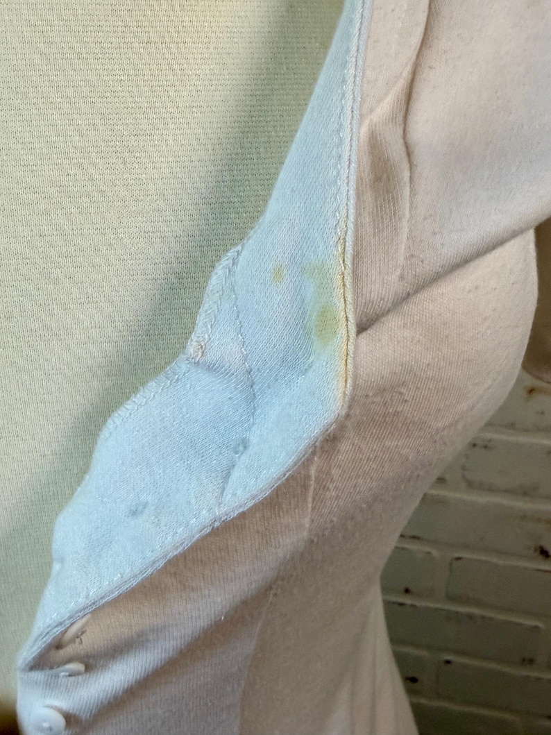 May include: Close-up of a light yellow and off-white long-sleeved shirt. The shirt has a buttoned placket and a light blue collar. There are yellow stains on the collar and sleeve. The fabric appears to be a soft knit.